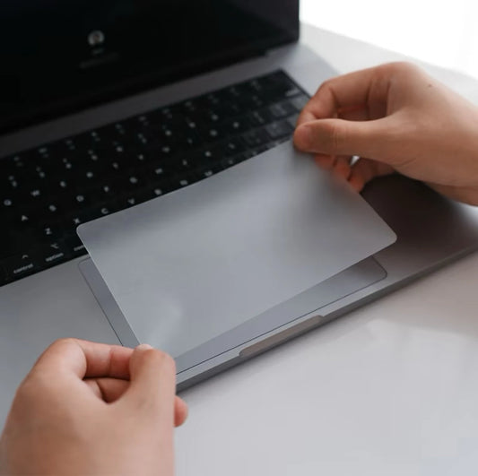hands applying clear matte film onto MacBook trackpad